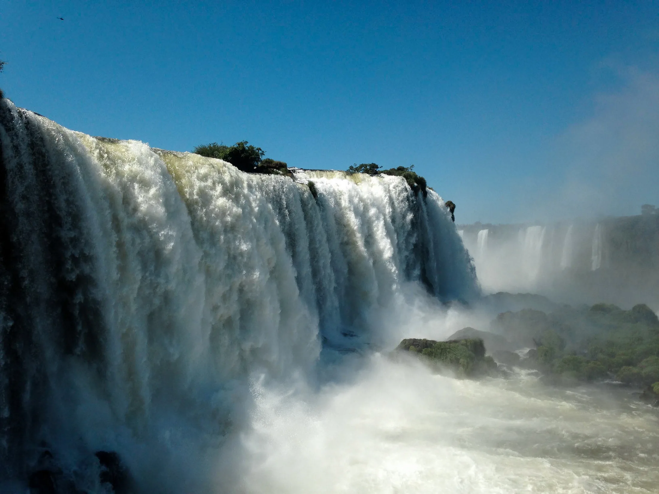 Multiple white curtains of Iguazu Falls drop through dense green Atlantic Forest.