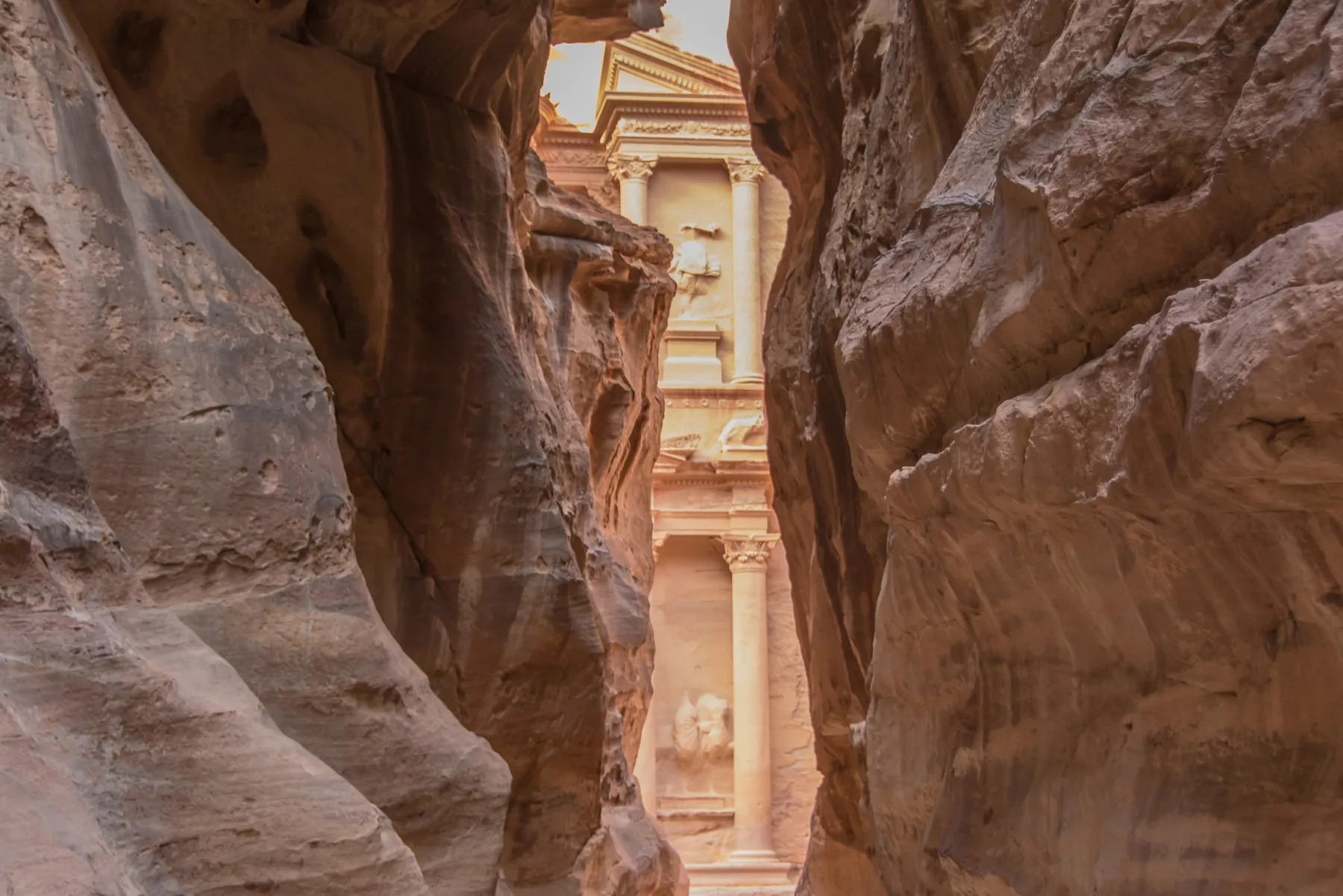 The carved facade of Al Khazneh appears between the high stone walls of the Siq at Petra.